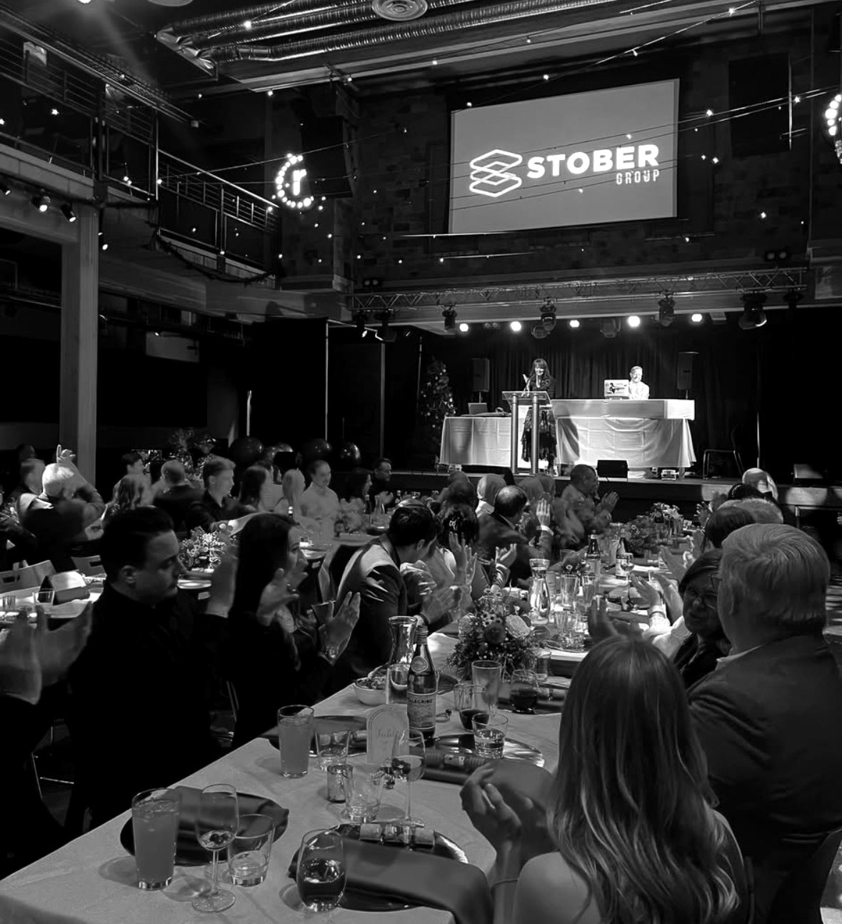 Guests applauding at a Stober Group gala dinner with the company logo on stage