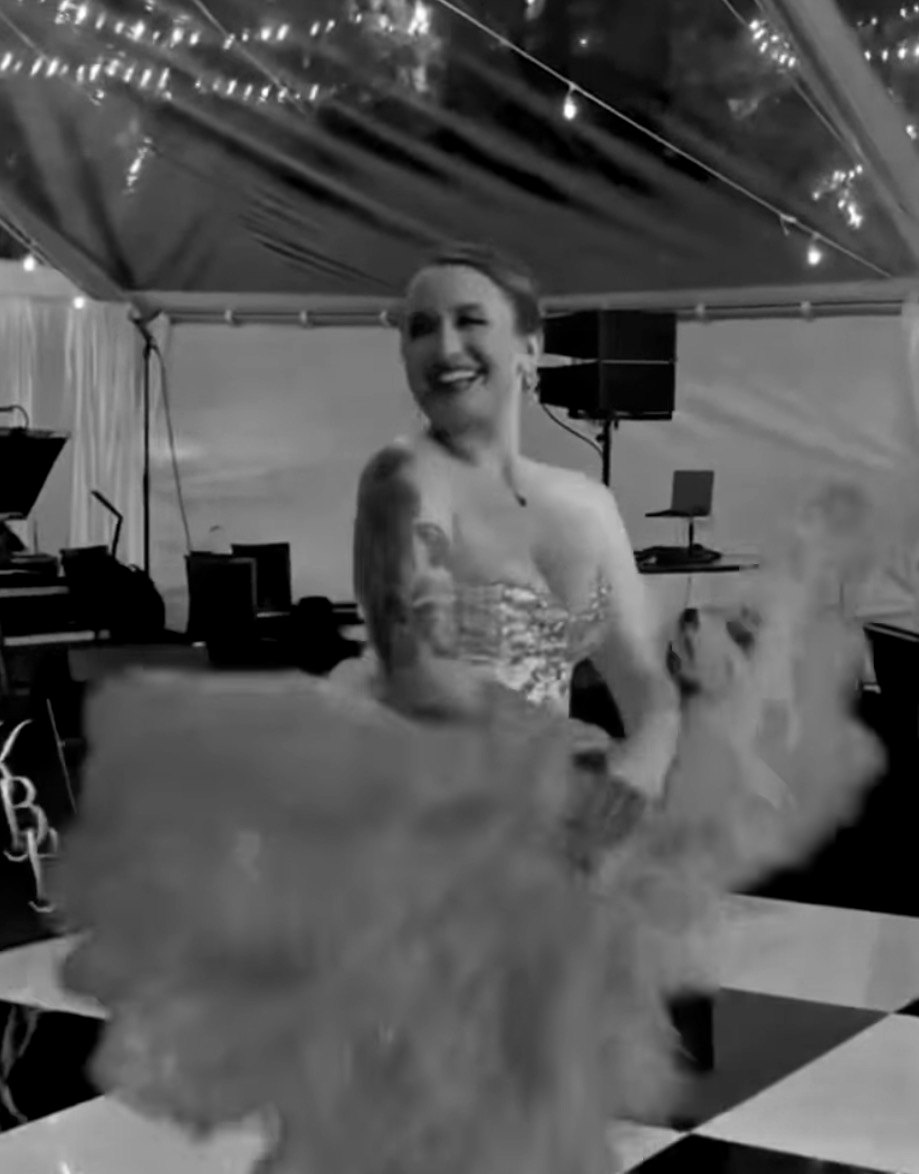 A performer with feather fans on a checkered dance floor under a lit tent